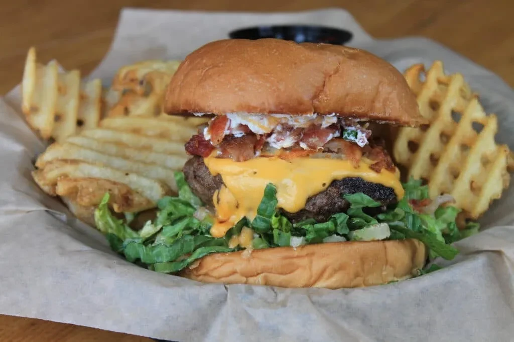 Loaded beef burger with cheese, bacon, sauce, and waffle fries.