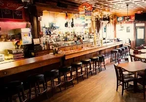 Empty, dimly lit rustic bar with a wooden counter and stools.