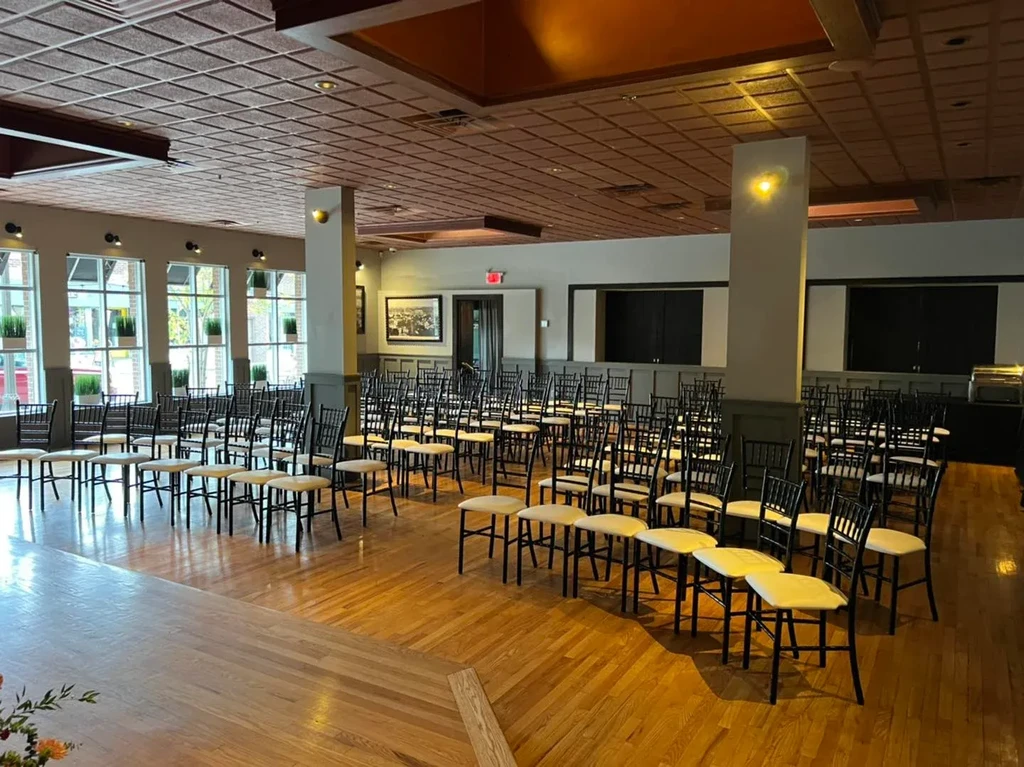An empty event space with stage, rows of chairs, and large windows.
