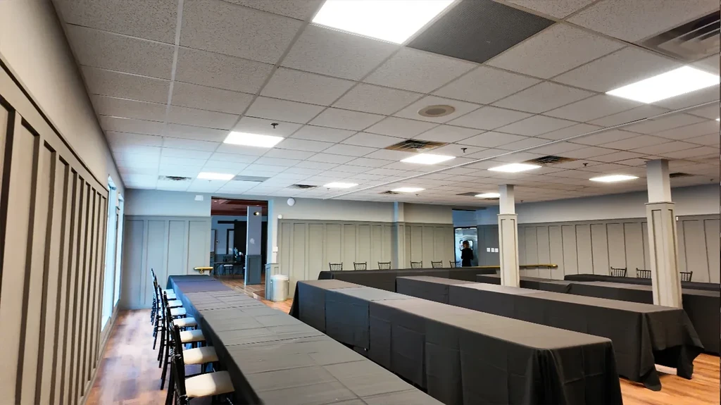 Prepared event hall with rows of black-draped tables on hardwood floors.