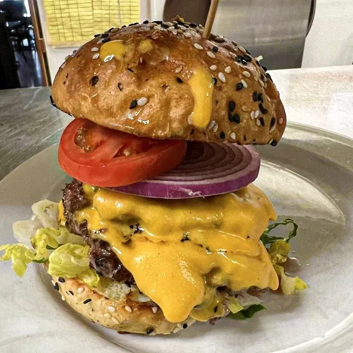 A stacked burger with two meat patties, melted cheese, and vegetables.