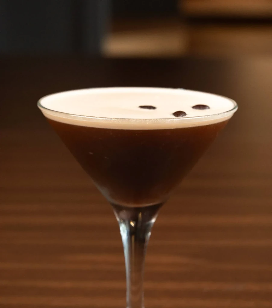 Martini glass with dark brown drink, creamy foam, and three coffee beans.