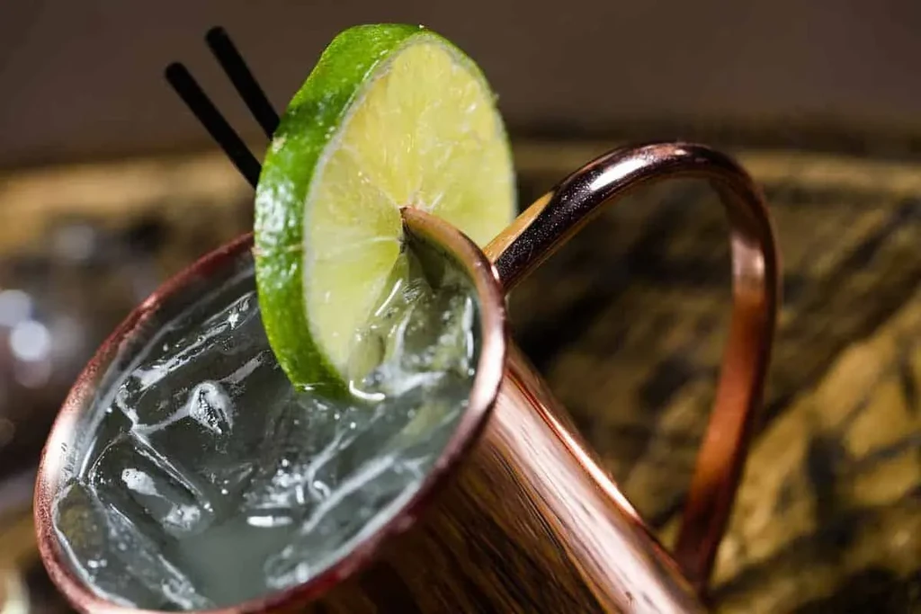Close-up, tilted copper mug cocktail with ice, lime, and straws.