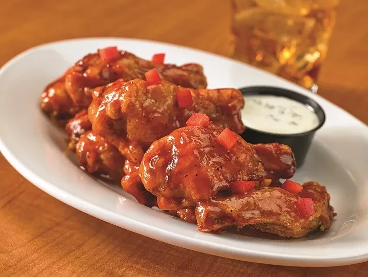 Chicken wings with reddish-orange sauce, diced peppers, and creamy dip.