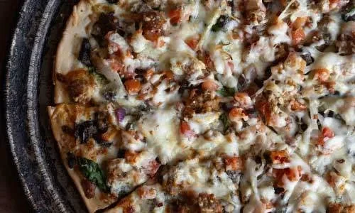 Freshly baked pizza with cheese, tomatoes, meat, and greens on a dark pan.
