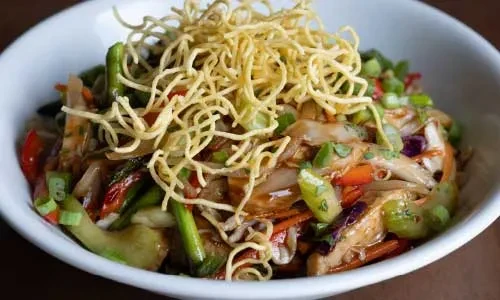 Vibrant stir-fry with crispy golden noodles and vegetables in a white bowl.