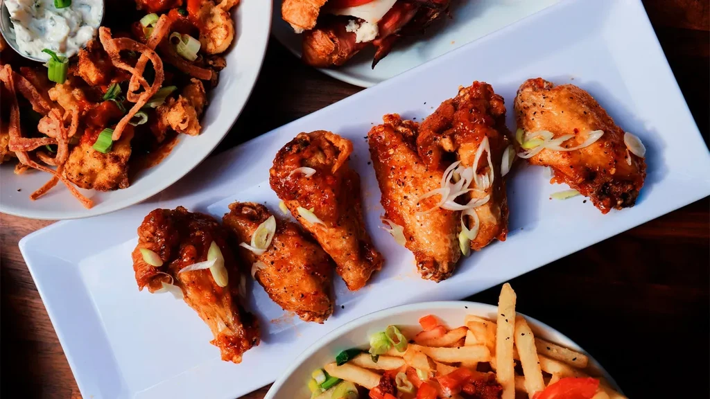 Various appetizers, including glazed chicken wings, on a dark wooden table.