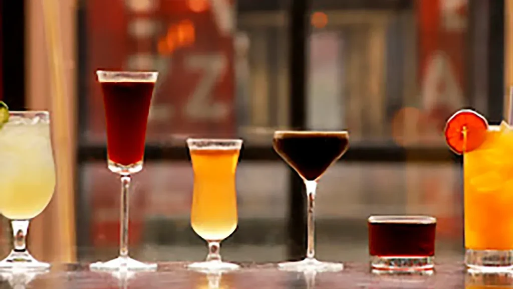 Six distinct cocktails in assorted glasses on a bar counter.