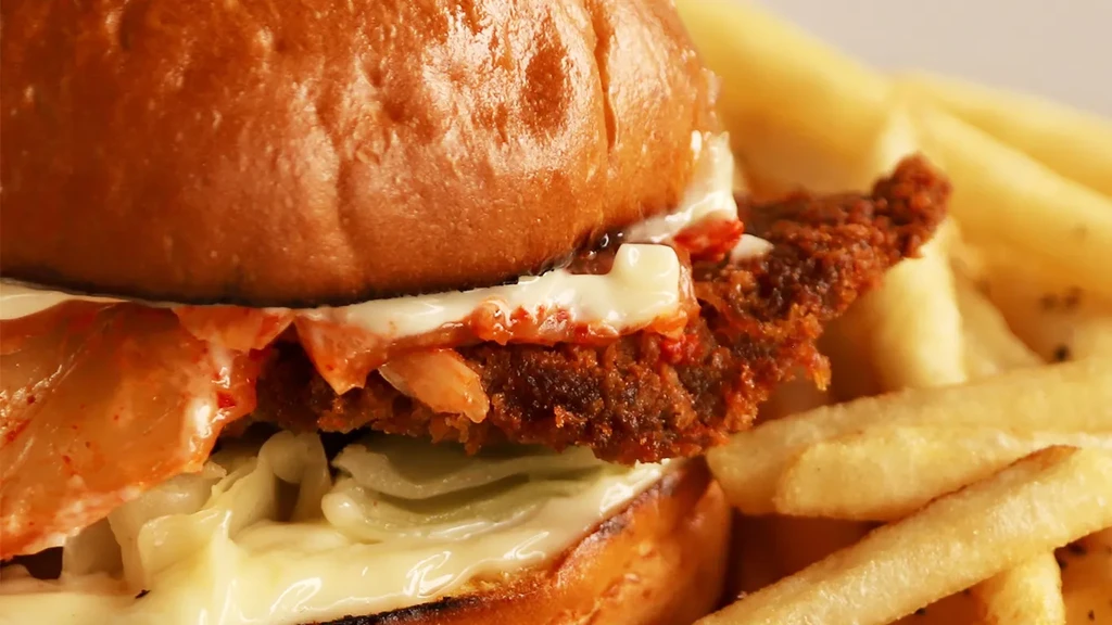 A burger with a crispy patty, brioche bun, kimchi relish, and fries.