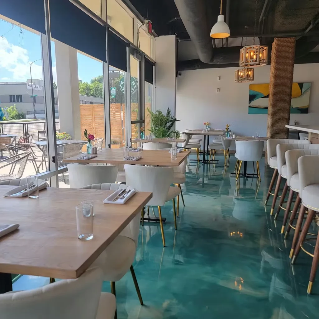 Modern restaurant interior with swirled turquoise epoxy floor, large windows.