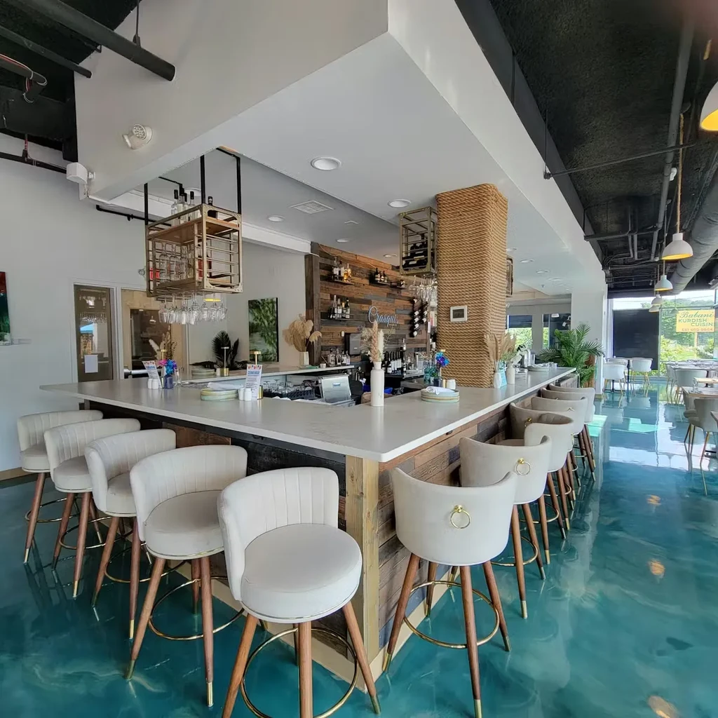 Modern bar interior with L-shaped counter, rustic wood, and teal floor.