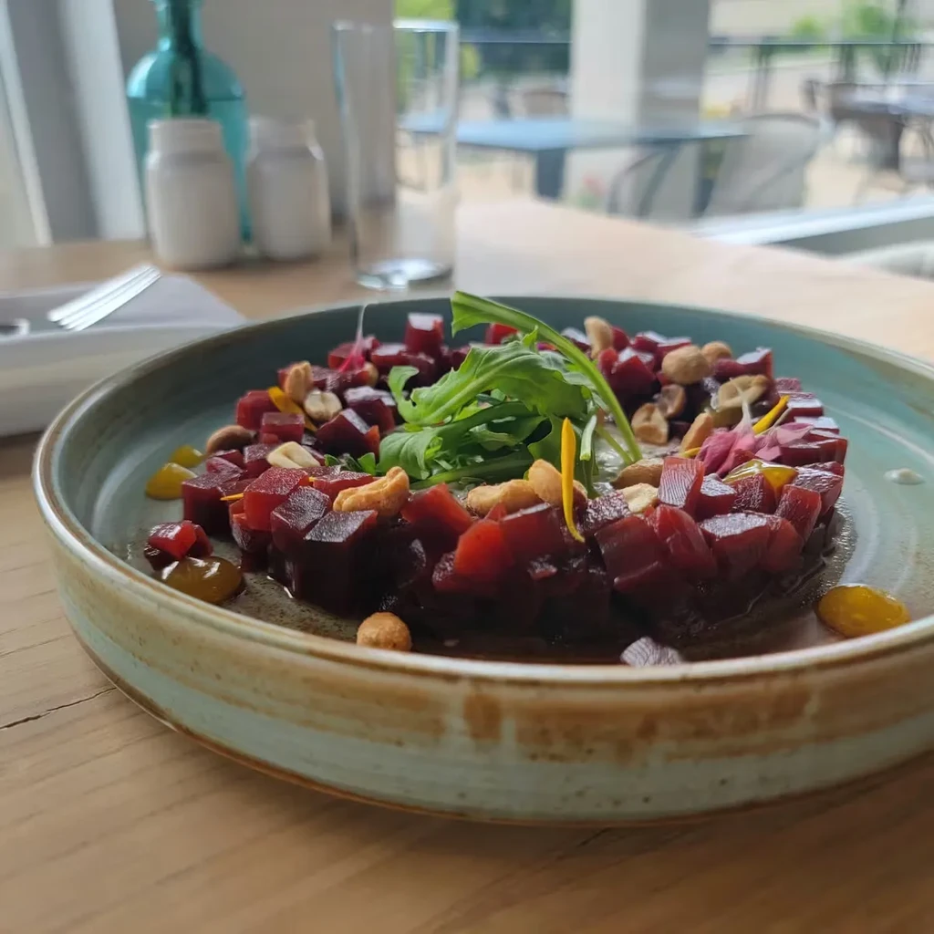 Beet tartare with arugula and cashews in a rustic blue bowl.