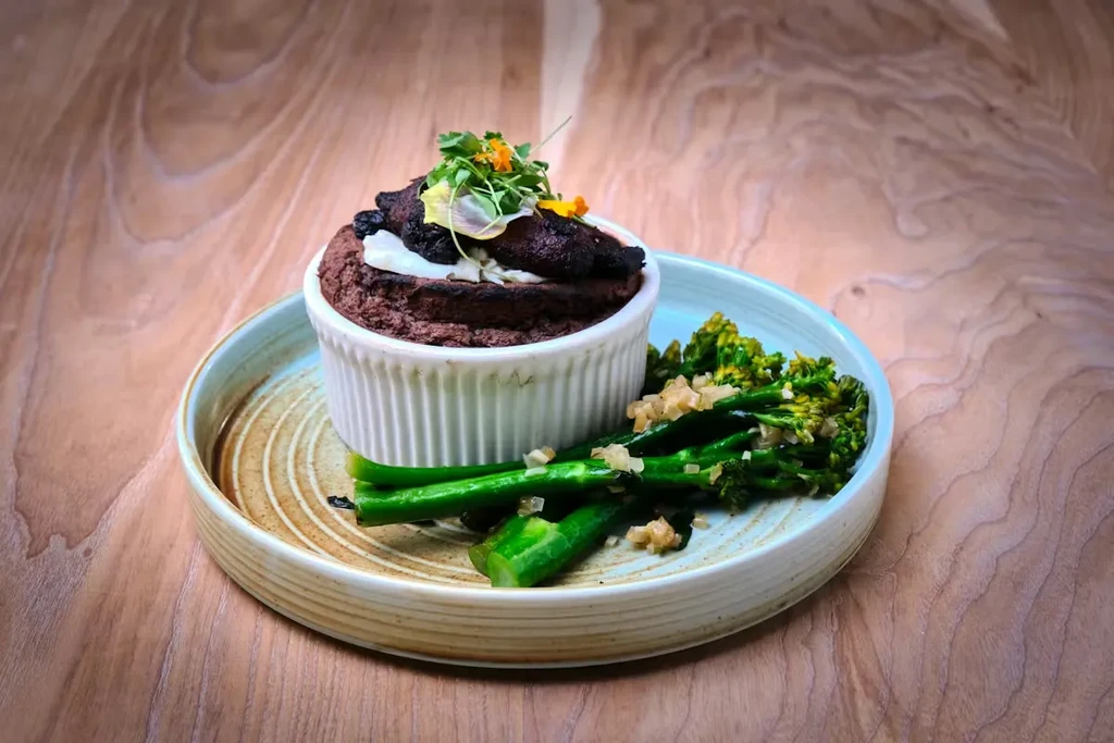 Baked dish in ramekin with broccolini, edible flowers on wood.
