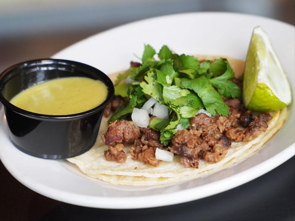Close-up of two street tacos with meat, cilantro, onions, lime, and salsa.