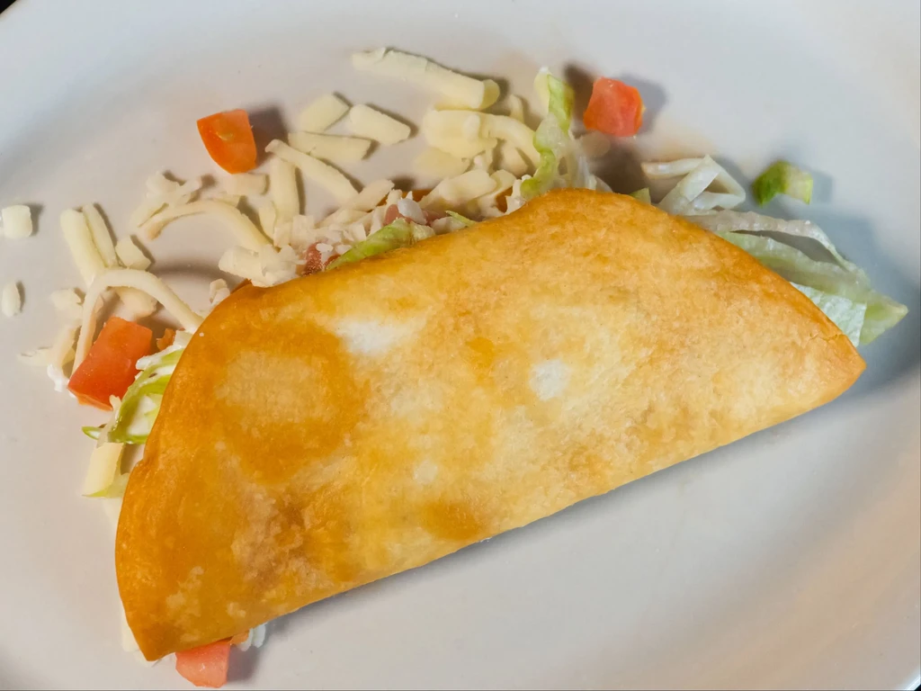 Overhead shot of a fried taco with lettuce, tomato, and cheese.