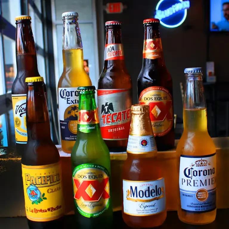 Eight cold Mexican beer bottles on a dark bar surface.