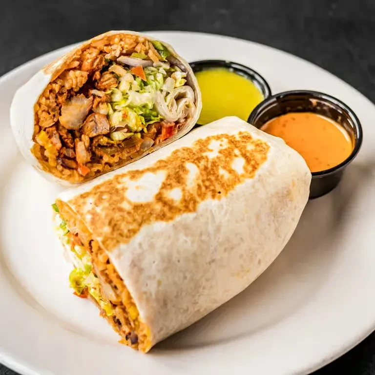 Two burritos, one cut open, showing filling, with two sauces.