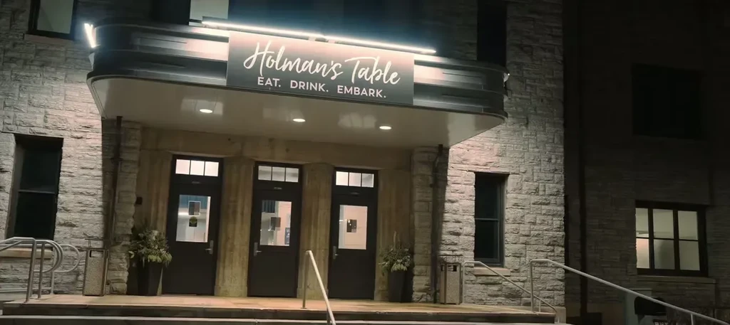 Holman's Table restaurant: stone facade, illuminated entrance and sign at night.