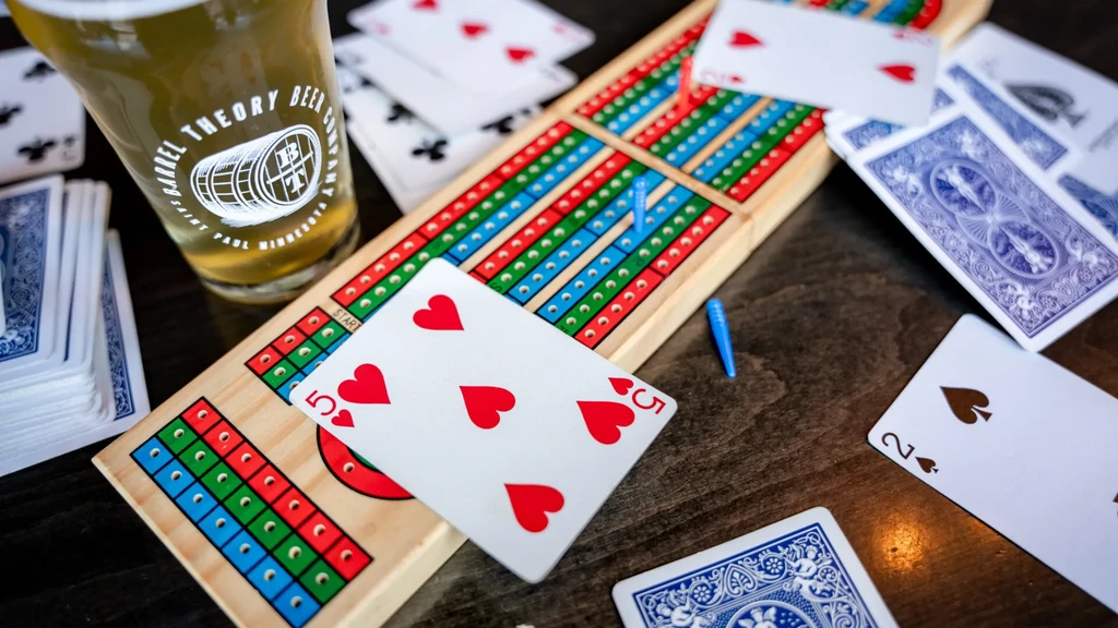 Overhead view of a cribbage game with cards, pegs, and beer.