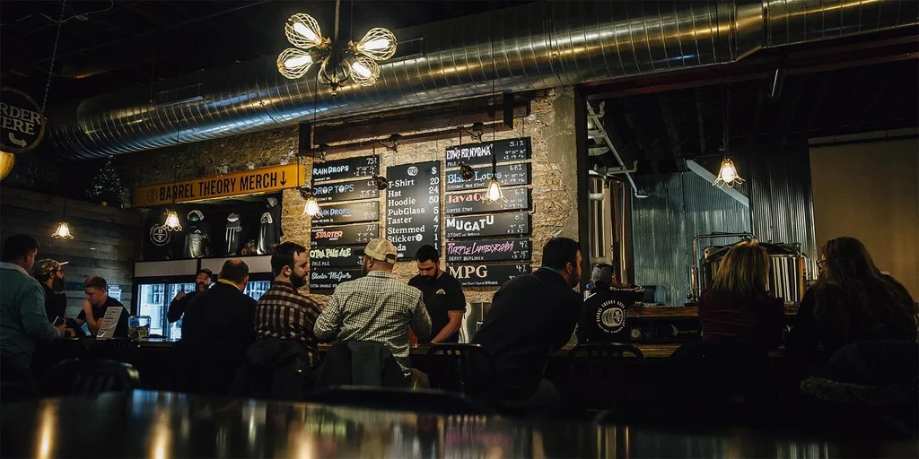 Brewpub bar interior showing patrons, exposed ductwork, and brick walls.