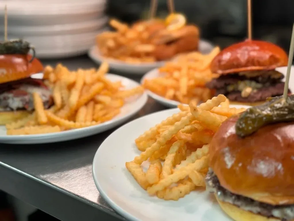 Multiple plates of mini-burgers with pickles and crinkle-cut fries.
