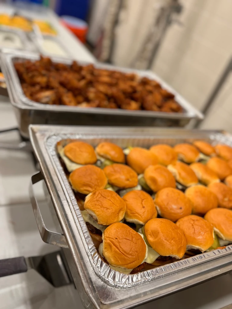 Catering trays with rows of sliders and fried chicken.
