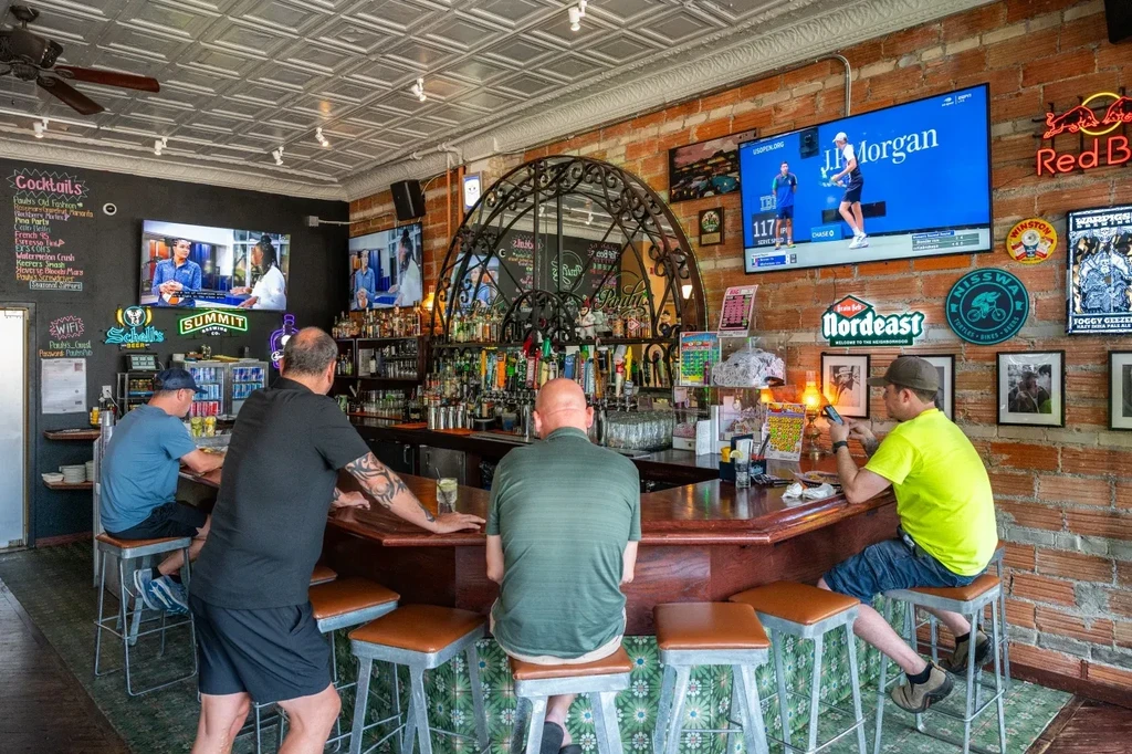 Patrons at a lively bar counter with TVs and neon signs.