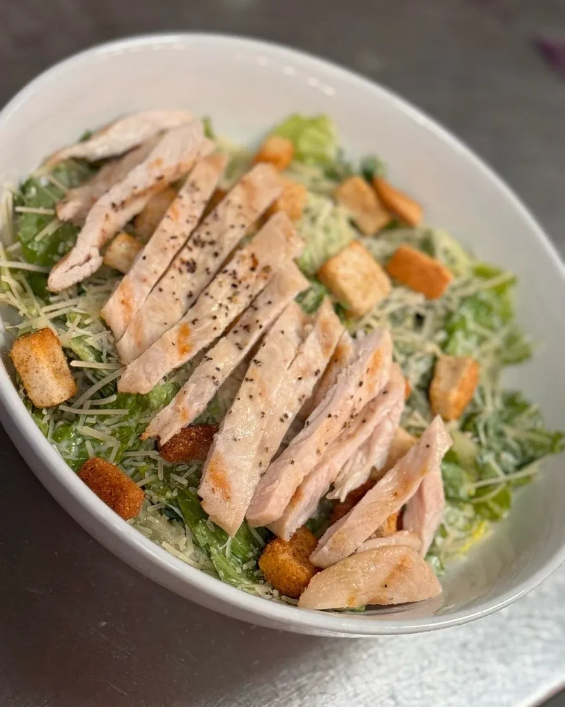 Grilled chicken Caesar salad in white bowl with croutons, parmesan.