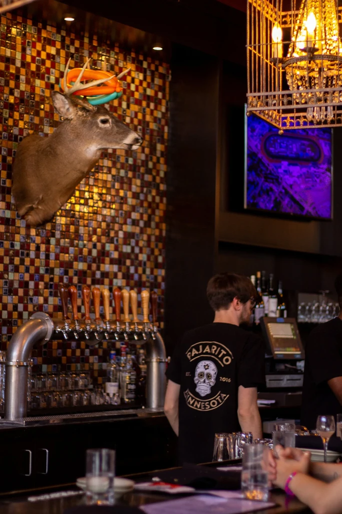 Vibrant bar with beer taps, mosaic wall, and ring-adorned deer head.
