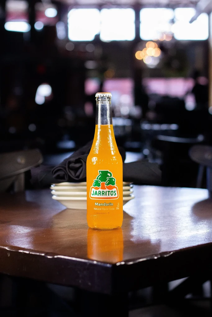 Orange Jarritos Mandarin soda bottle on dark wood, blurred background.