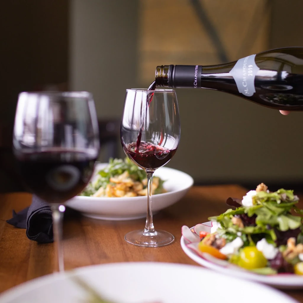 Red wine actively pouring from bottle into a glass.