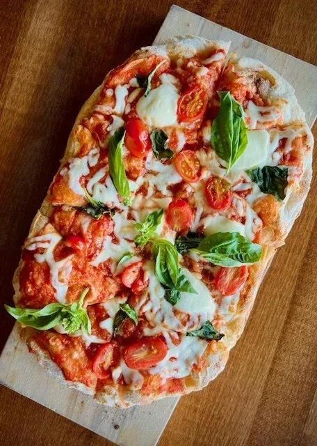 Overhead shot of focaccia pizza with tomato, mozzarella, basil, cherry tomatoes.