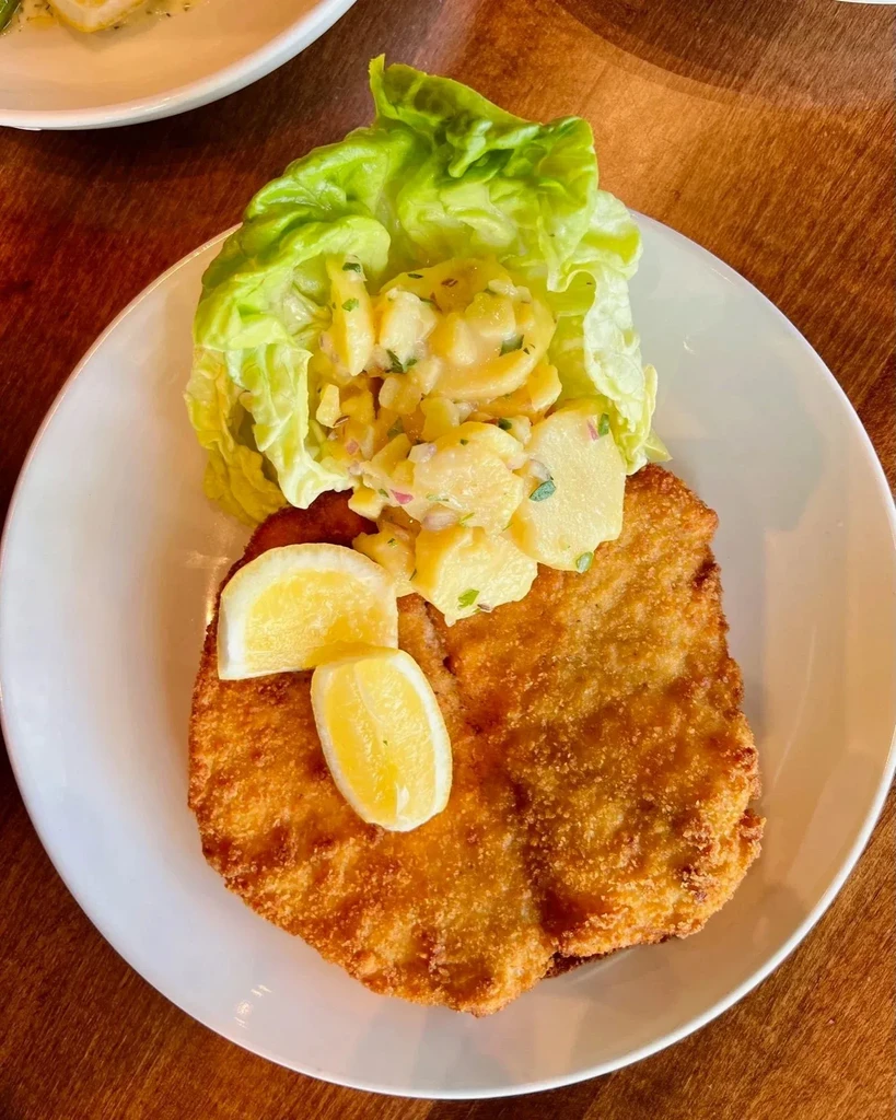 Golden-brown breaded cutlet with lemon, lettuce, and chunky potato salad.