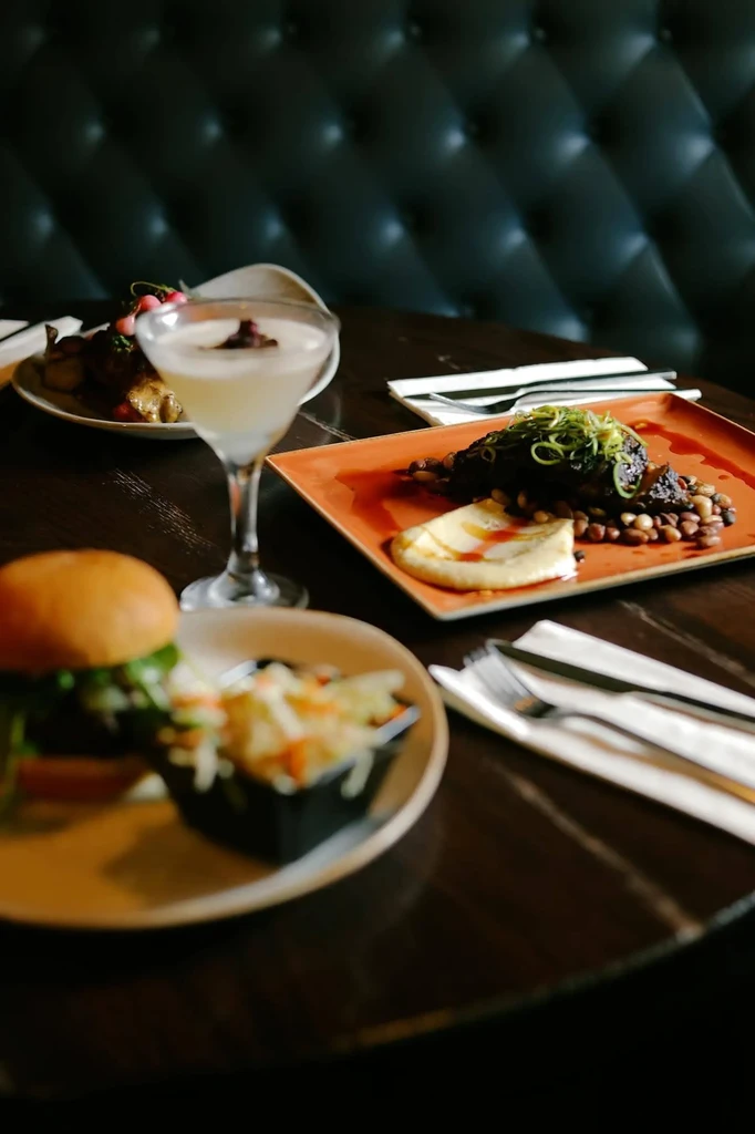 Cocktail, burger, and main course on a dark table in a restaurant.