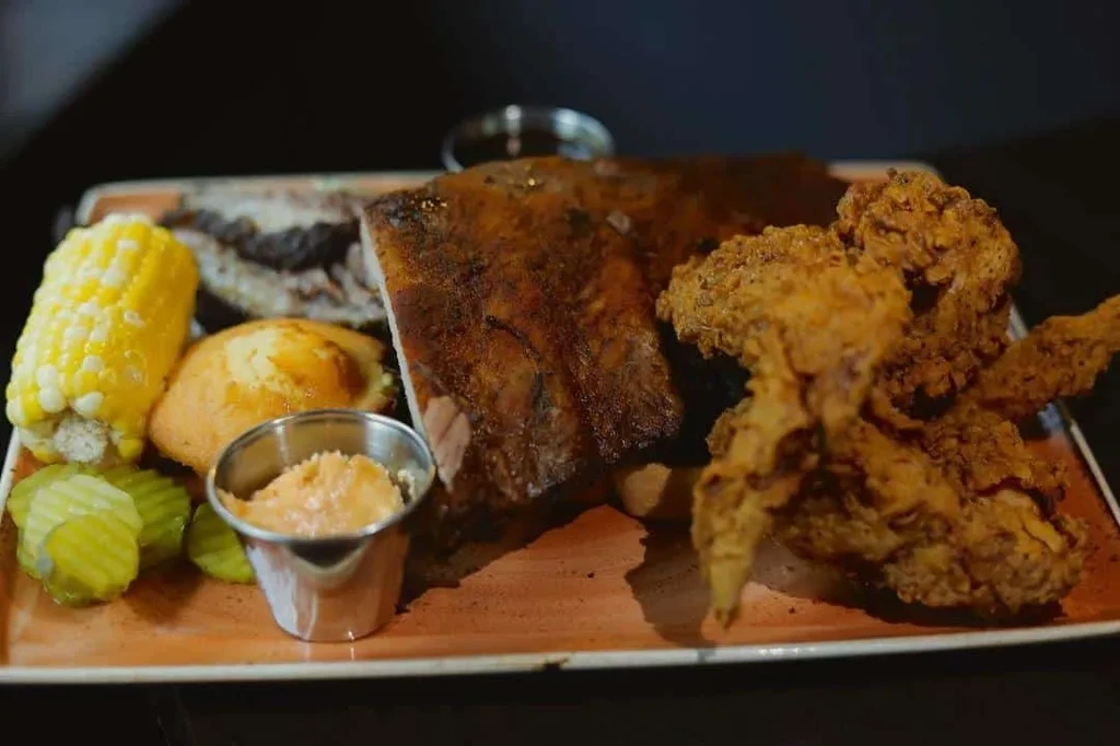 Rustic plate with BBQ ribs, fried chicken, corn, cornbread, and pickles.
