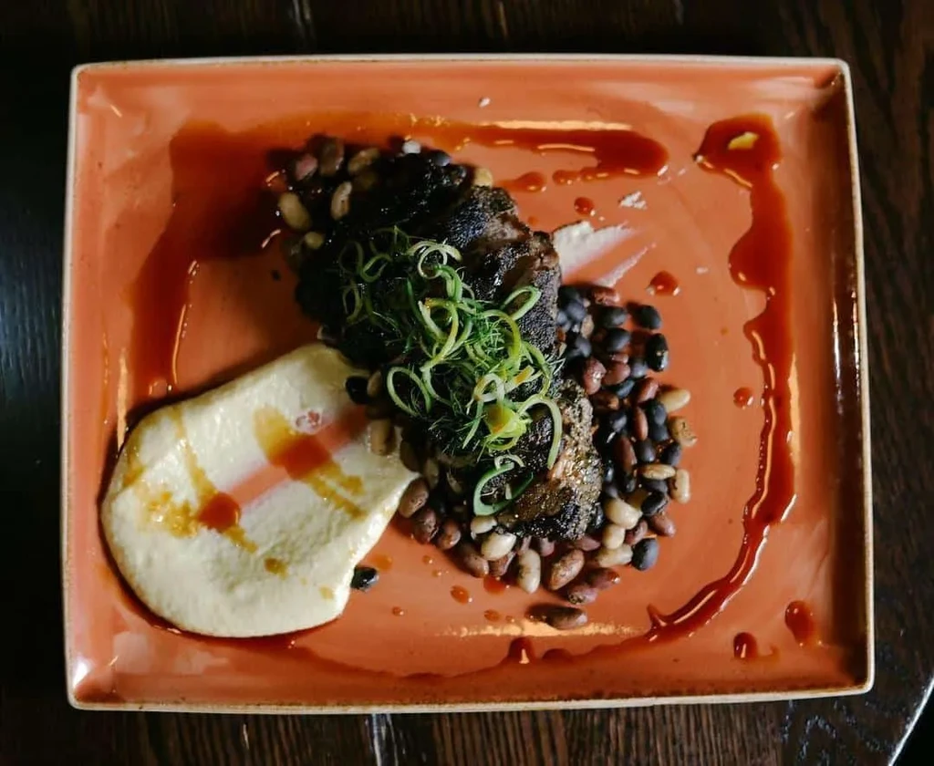Overhead view of artfully plated dark meat, puree, beans, herbs.