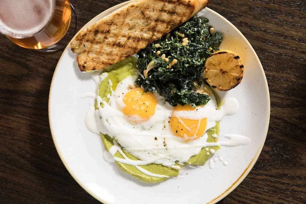 Overhead view of plated eggs, greens, toast, lemon, and beer.