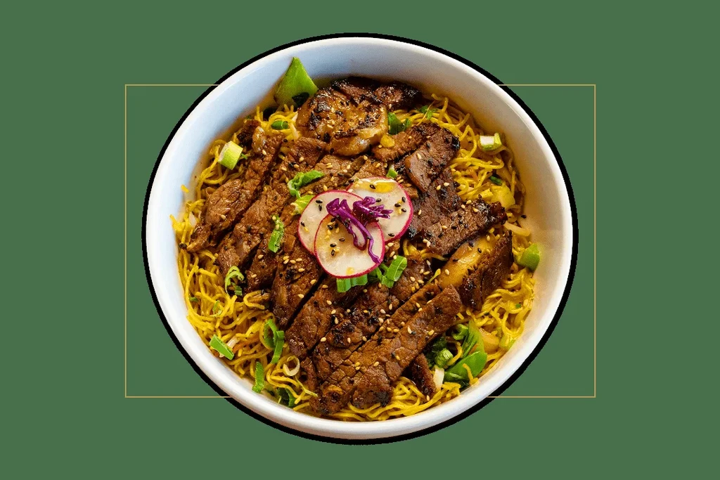 Noodle bowl with grilled meat, radish, red cabbage, and garnishes.