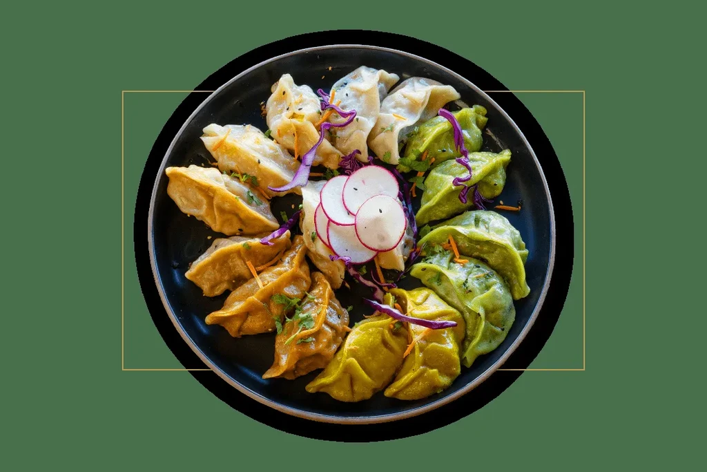 Assorted colorful dumplings garnished with vegetables on a dark plate.