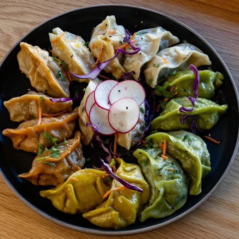 Colorful dumplings on a black plate, garnished with cabbage, carrots, cilantro, radishes.