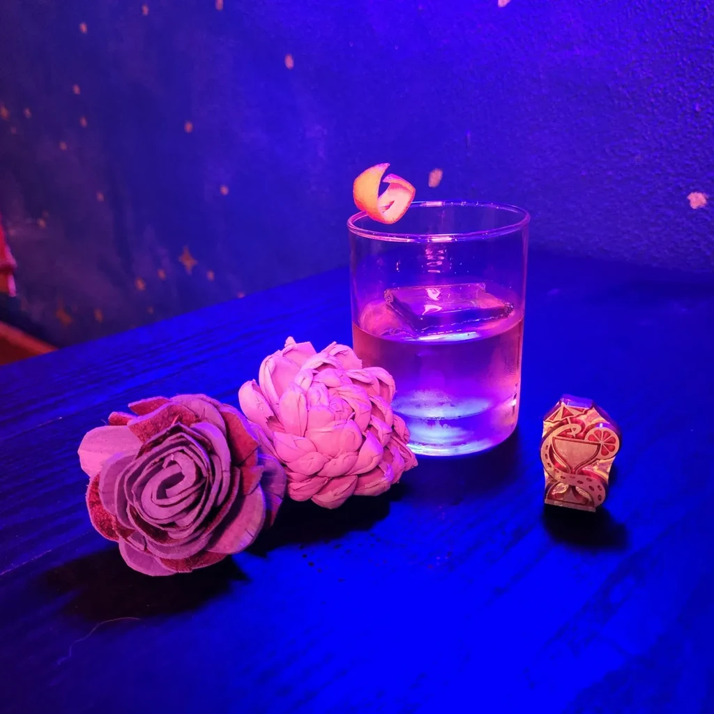 Cocktail with orange peel under dramatic blue and purple lighting.