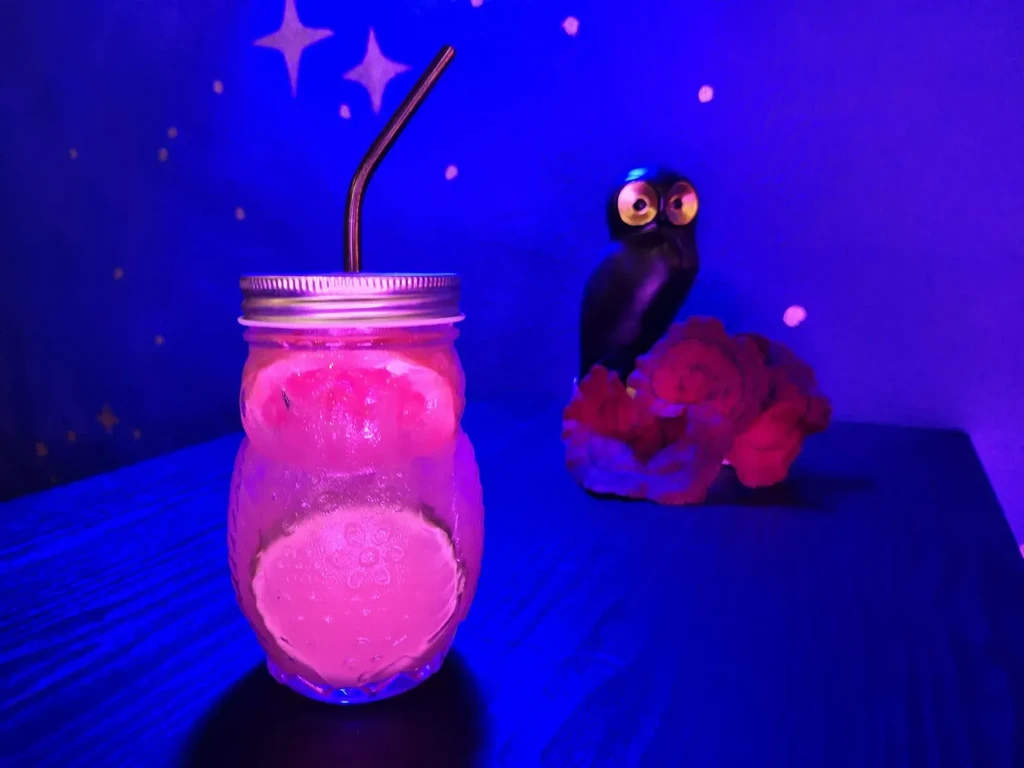 Pink drink in owl glass, ceramic owl, glowing coral, starry background.