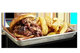 Pulled pork sandwich with crispy golden potato wedges on a tray.