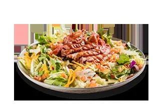 Large salad with steak, mixed greens, cheese, and tomatoes in a bowl.