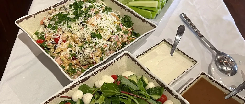 Colorful pasta salad, green salad, dips, and celery on a buffet.