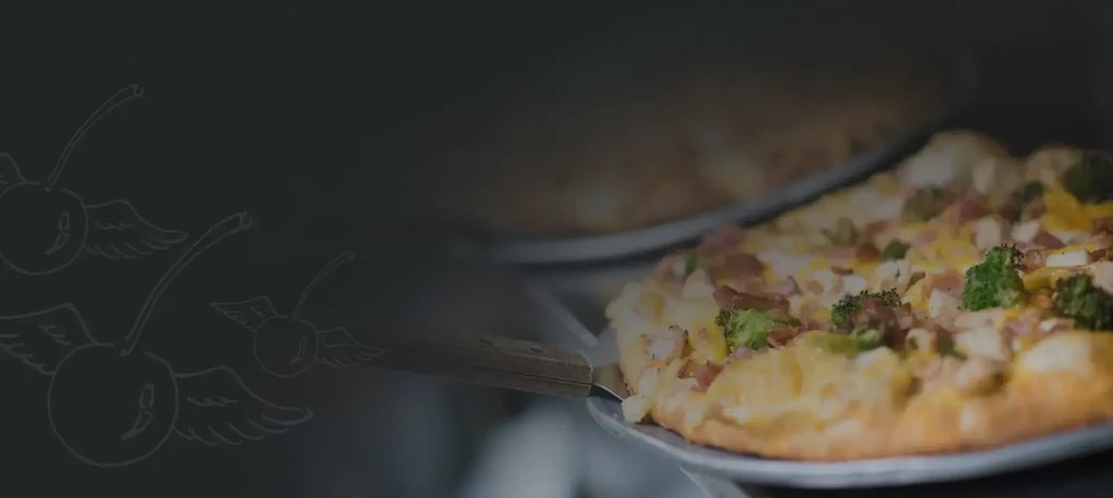 Pizza with melted cheese, broccoli, and meat slid from oven on peel.