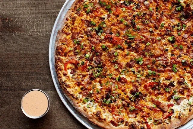 Pizza with melted cheese, meats, peppers, and green onions on a pan.