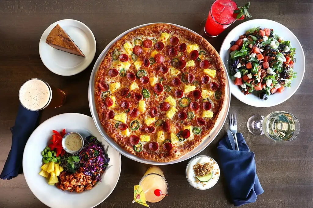 Overhead view: pizza centerpiece surrounded by diverse food and drinks.
