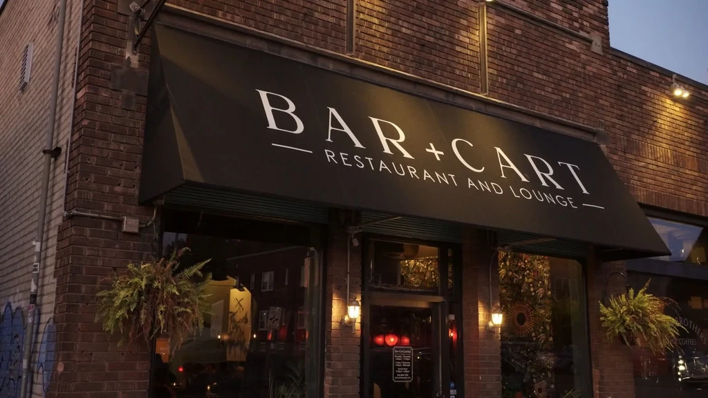 Red brick BAR + CART entrance with black awning, lit at dusk.