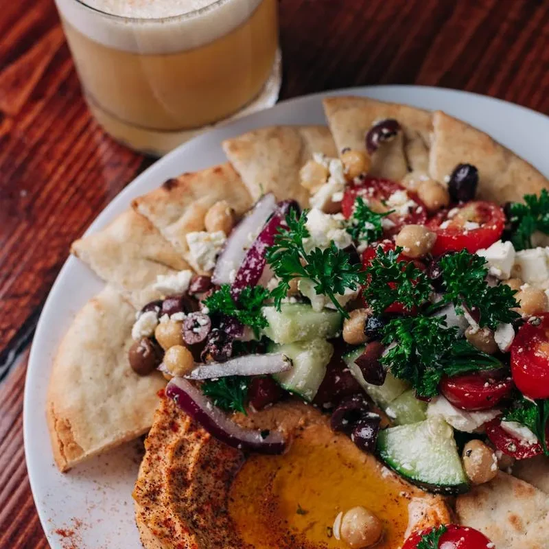 Colorful Mediterranean platter with hummus, pita, salad, and drink.